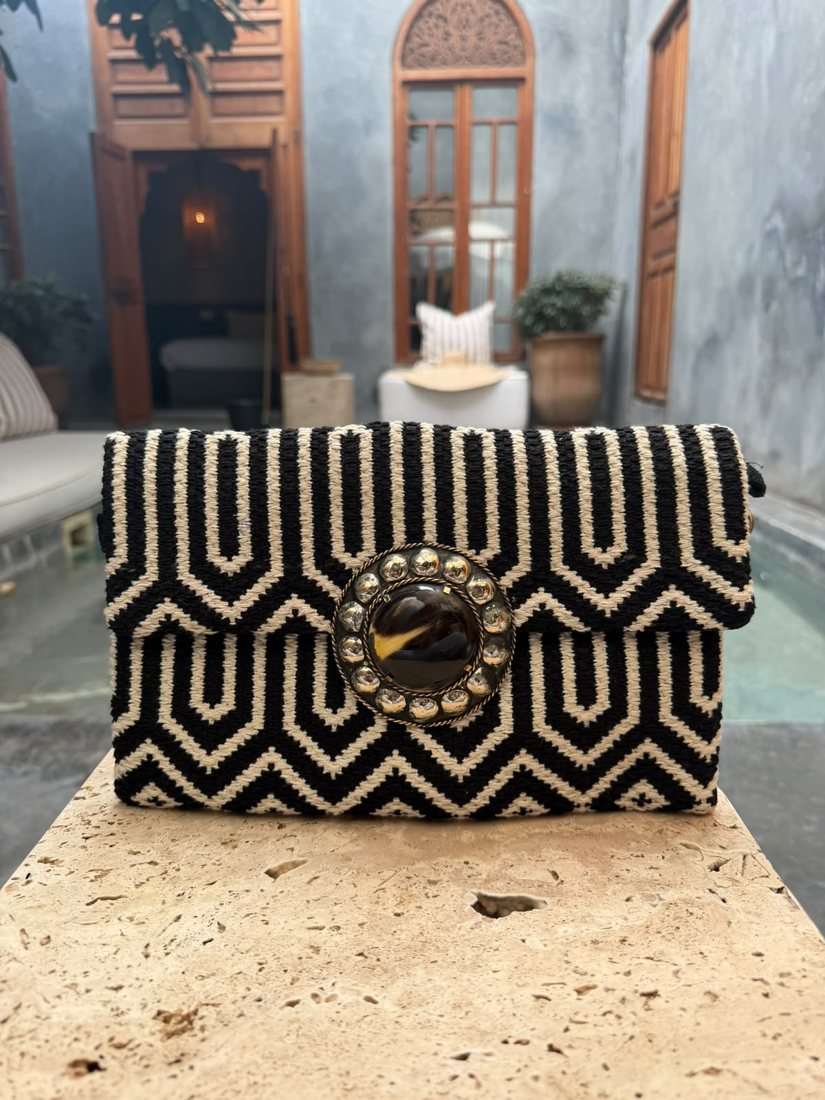 Black-and-cream geometric carpet bag with a dark circular centrepiece and metallic surround, photographed in a courtyard