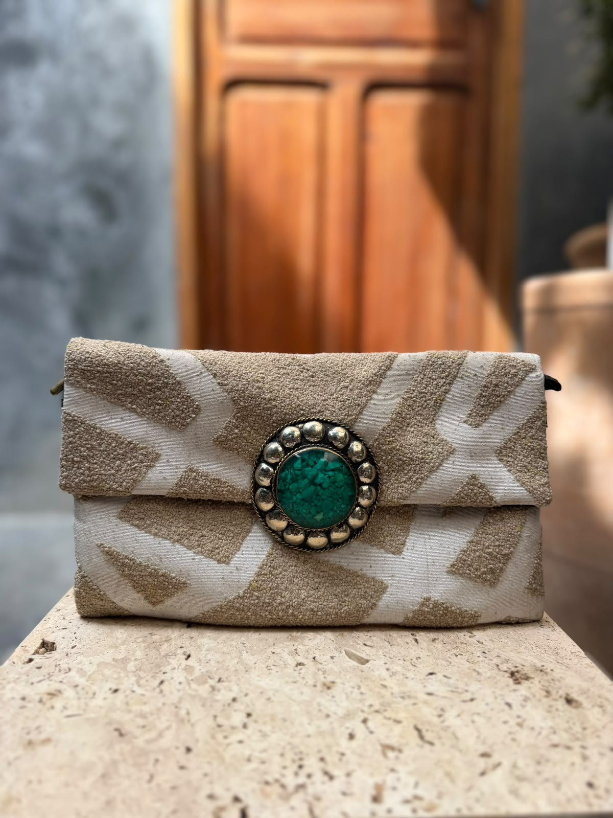 Cream carpet bag with raised beige abstract patterns and a green circular centrepiece framed by metallic detailing