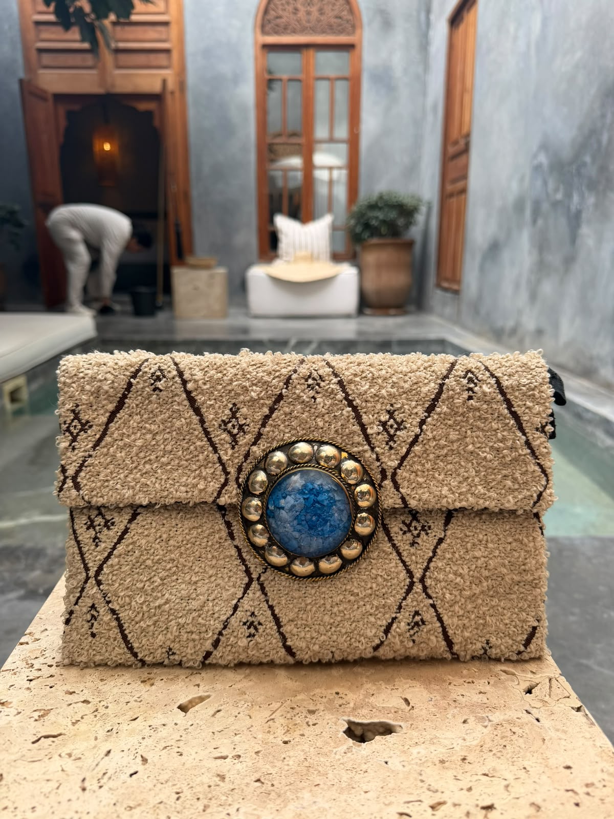 Beige textured carpet bag with dark diamond motifs and a blue circular centrepiece with metallic surround