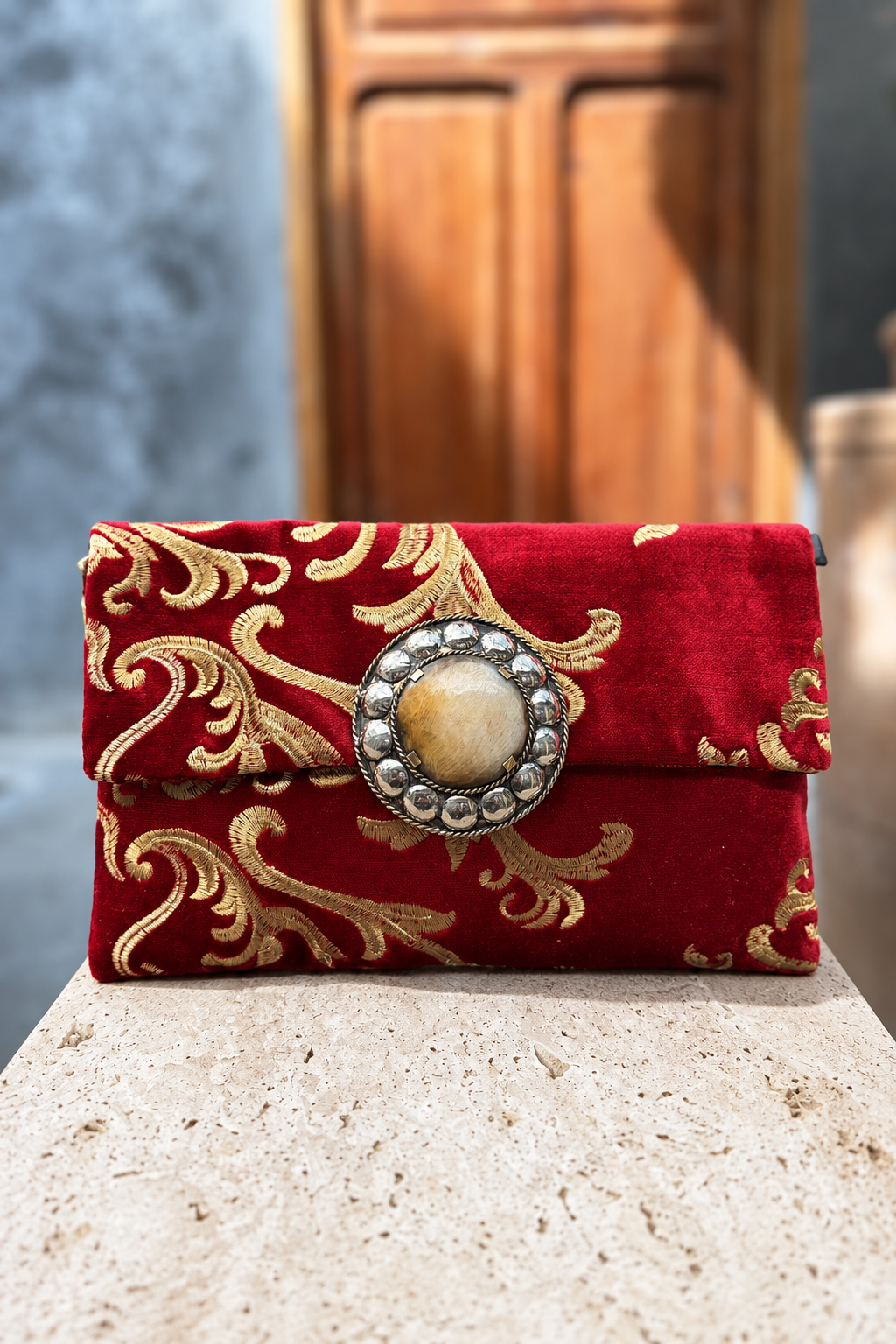Red Velvet Legzita red-and-gold carpet bag on a beige stone pedestal in front of a wooden doorway