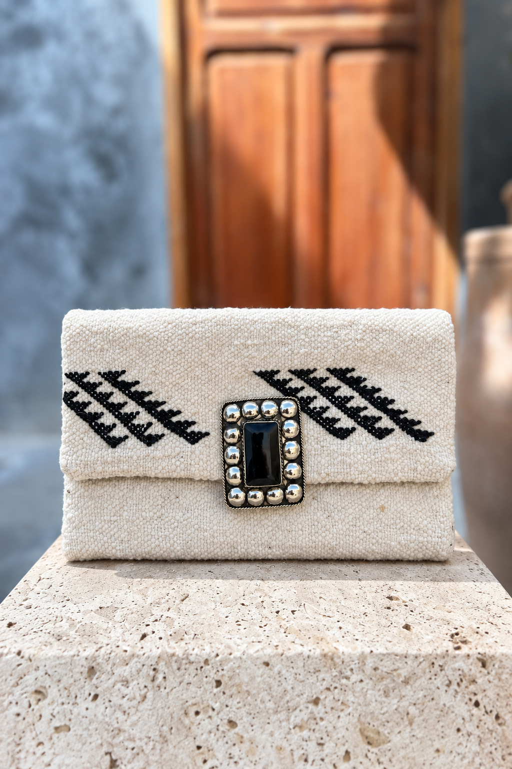 Legzita Blanche ivory carpet bag with black motifs and rectangular black centrepiece on a beige stone pedestal in front of a wooden doorway