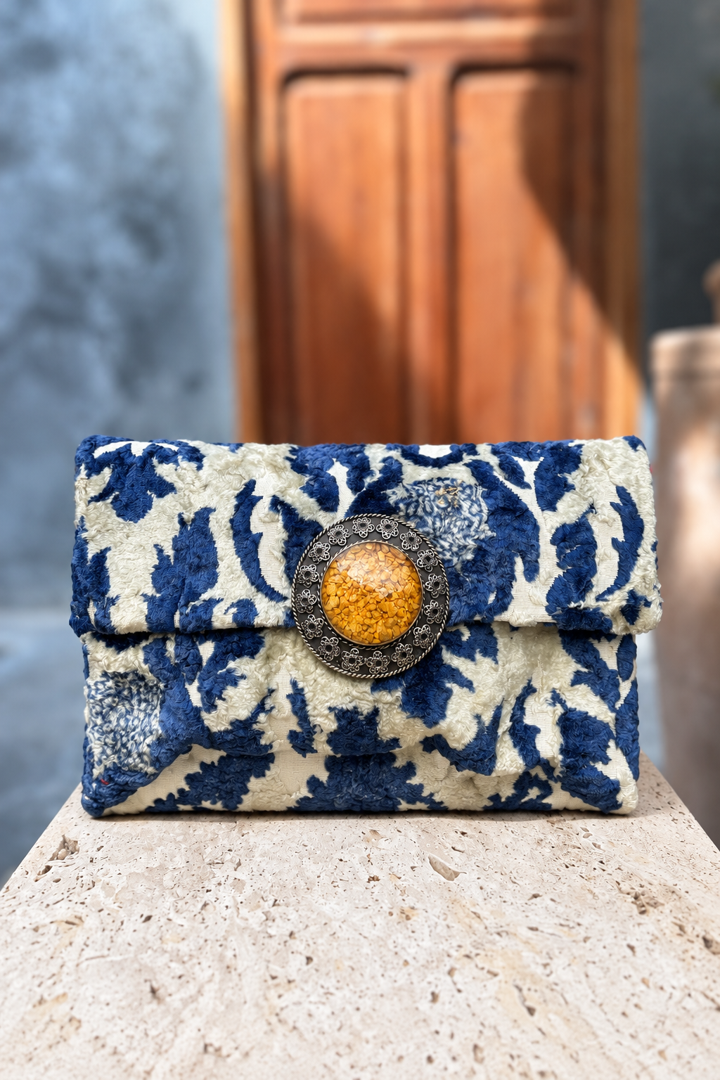 Sky Silver Bag with blue-and-ivory floral textile and yellow centrepiece on a beige stone pedestal