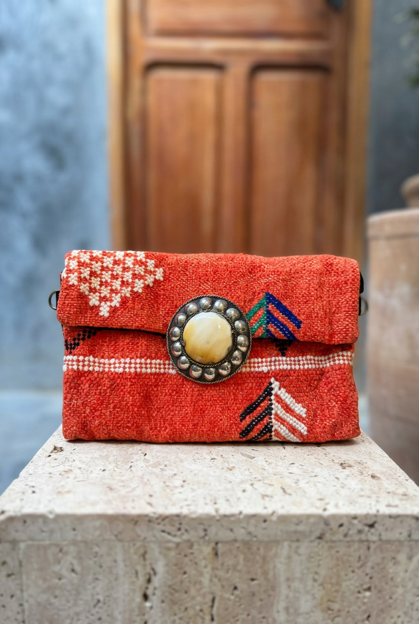 Coral woven carpet clutch with cream details and a pale centrepiece on a stone ledge