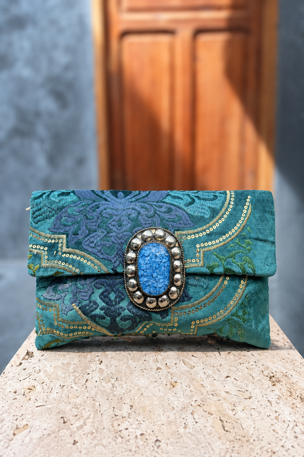 Turquoise paradise carpet bag with blue oval centrepiece on a beige stone pedestal in front of a wooden doorway